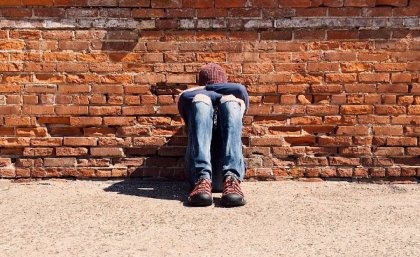 Person with head in their hands against red brickwall.